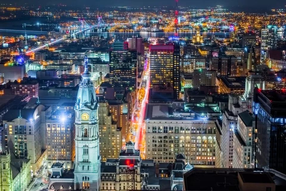 Aerial Philadelphia cityscape by night with the City Hall tower in the foreground and Ben Franklin bridge spanning Delaware river in the back